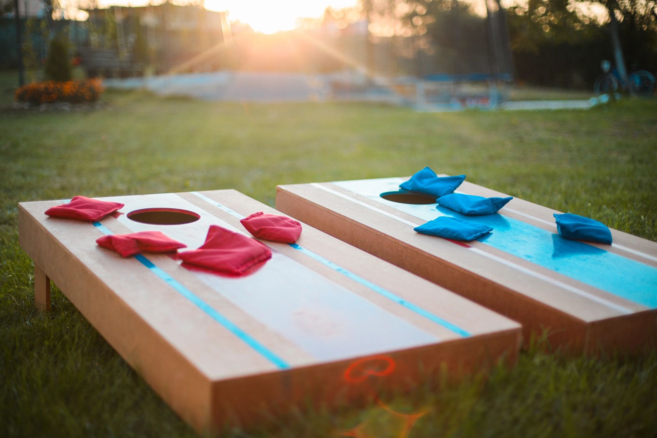 Two cornhole boards on grass with red and blue bean bags at sunset.