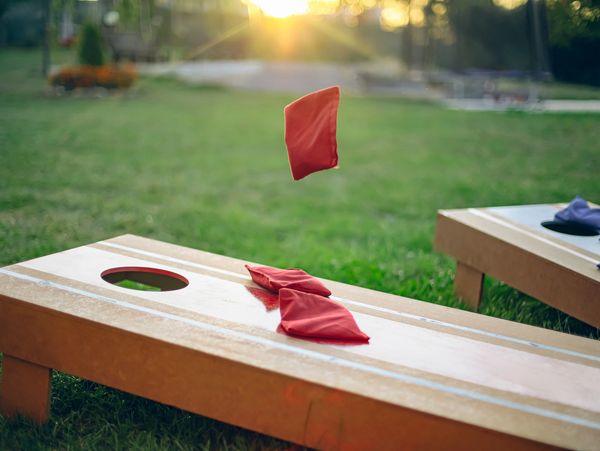 Cornhole bean bags in mid-air over board at sunset.