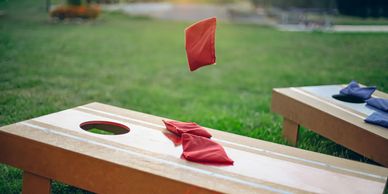 Red bean bag mid-air above cornhole board during sunset in a backyard.