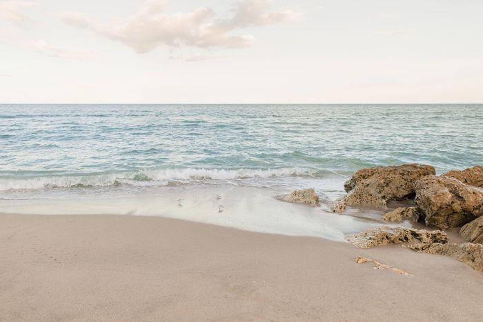 Calm beach scene with gentle waves, sandy shore, and rocky outcrops under a soft sky.
