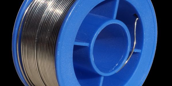 Spool of shiny solder wire with blue plastic holder on black background.