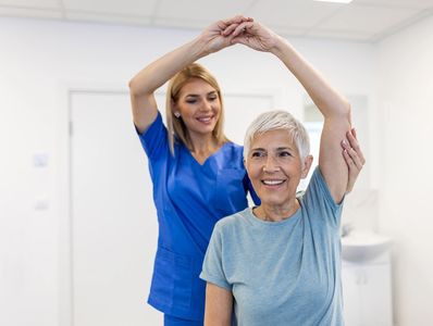 Therapist assists elderly woman with arm stretch.