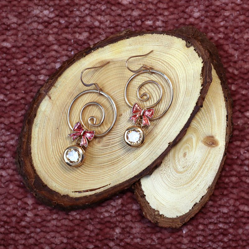 Golden colored handmade earrings on wooden slabs on brown textured fabric background close up