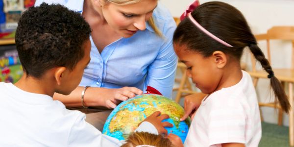 Teacher and children exploring a globe in a classroom.