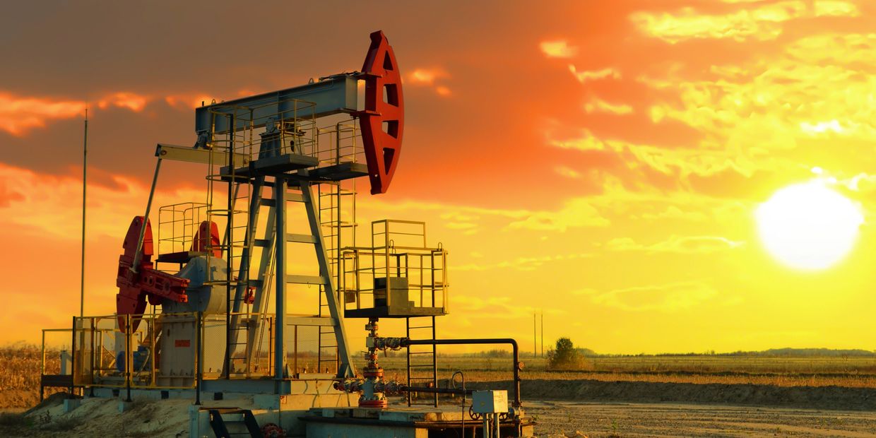 Oil pumpjack operating in a field during a vibrant sunset.