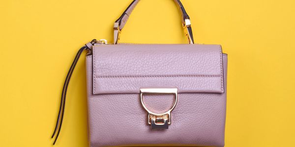 A stylish lavender handbag with a gold clasp on a yellow background.
