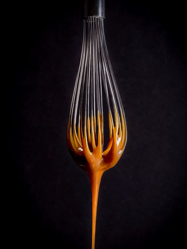 Whisk coated with dripping caramel against a dark background.