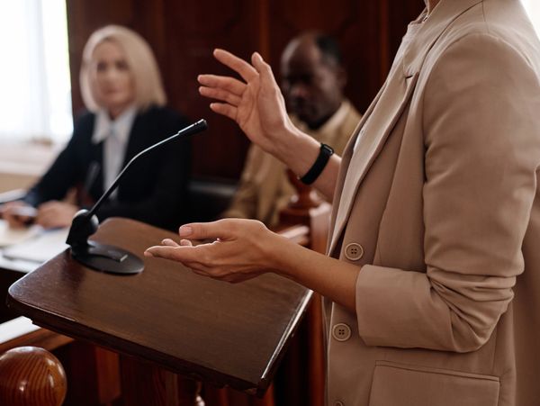 A person presenting a case at a courtroom podium with attentive listeners.