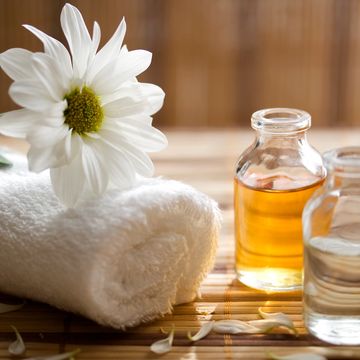Rolled white towel with a daisy and two bottles of essential oils on a wooden surface.
