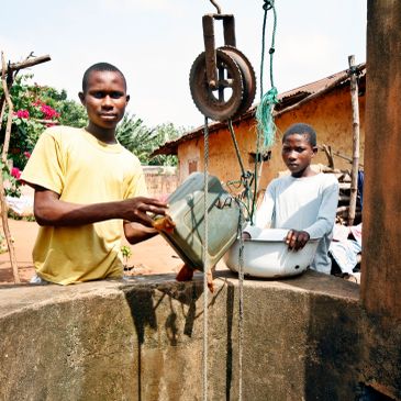 Two boys collecting water from a well using containers.