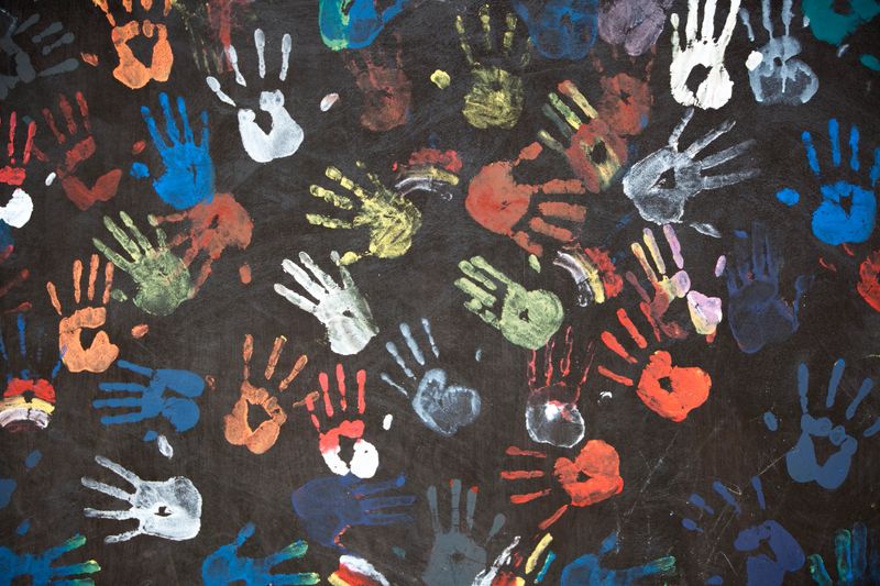 "colorful children's handprints on a textured black wall - fragment of a busstop wall in Bali, Indonesia"