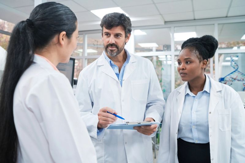 Mature male scientist discussing over clipboard with female colleagues at laboratory