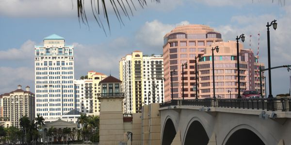 City skyline with modern buildings and a bridge under a partly cloudy sky.