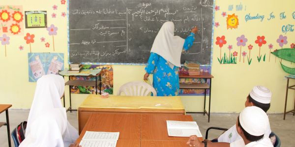 Teacher writing on blackboard with students in classroom.