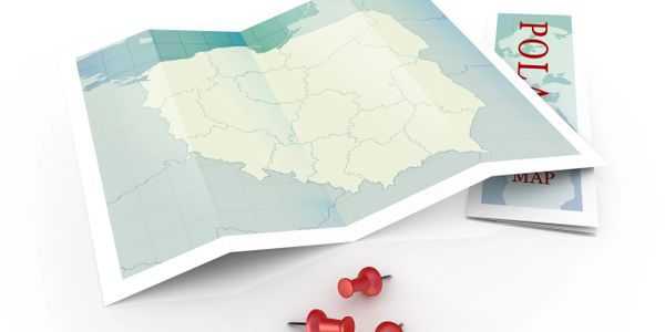 Folded map of Poland with three red push pins on a white surface.