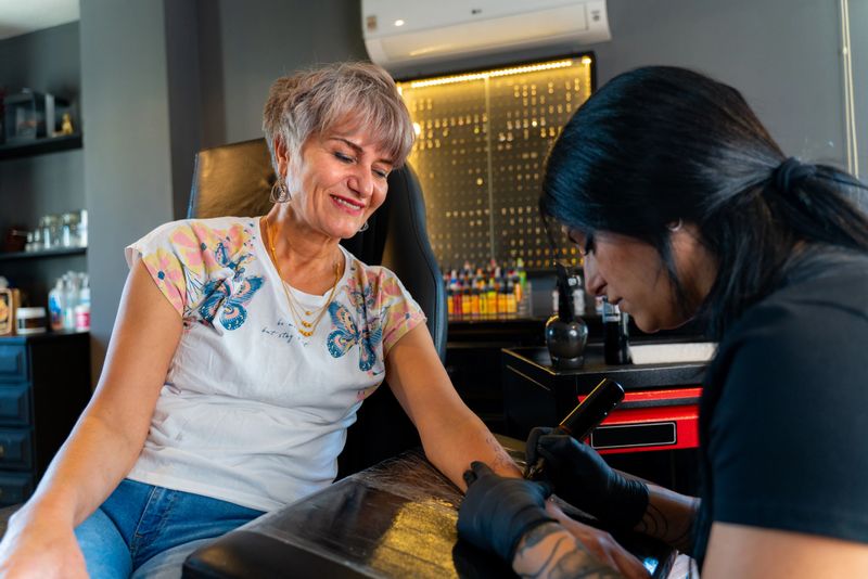 female tattoo artist, tattooing the female senior adult customer in her tattoo studio