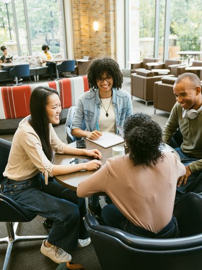 Group of four diverse young adults chatting at a table indoors.