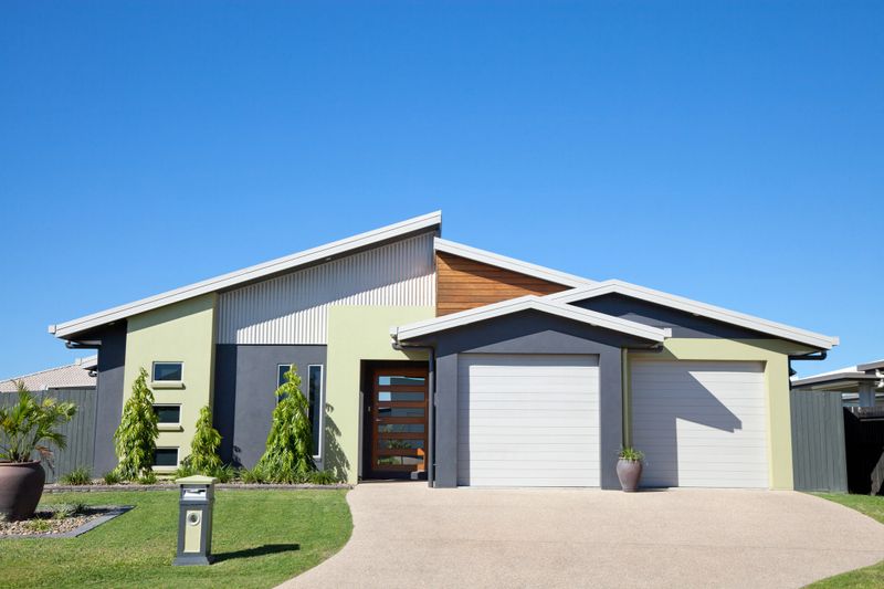 Front of a new neat modern single story family home with landscaped gardens, green grass and blue sky for copy space.