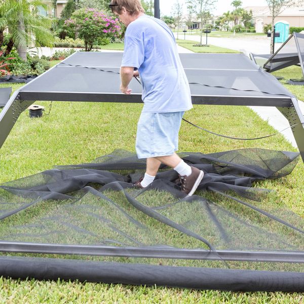 Man assembling a trampoline outdoors on a lawn.