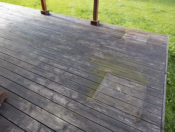 Partially cleaned wooden deck with two square patches and green grass background.