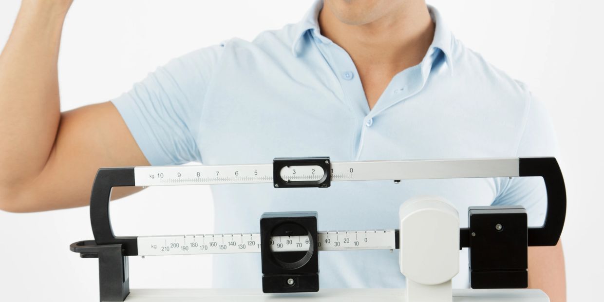 Man showing muscle while standing behind a balance beam scale.