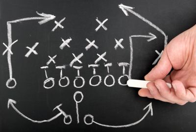 Hand drawing a football play strategy on a chalkboard.