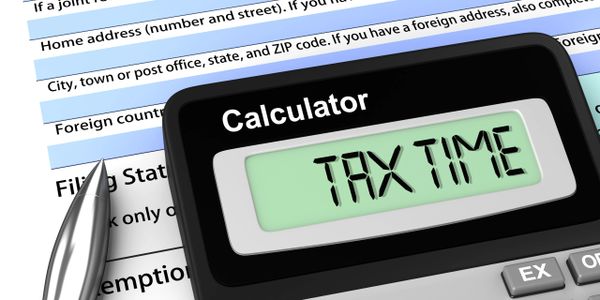 Calculator displaying 'TAX TIME' on top of a U.S. tax form 1040 with a pen.