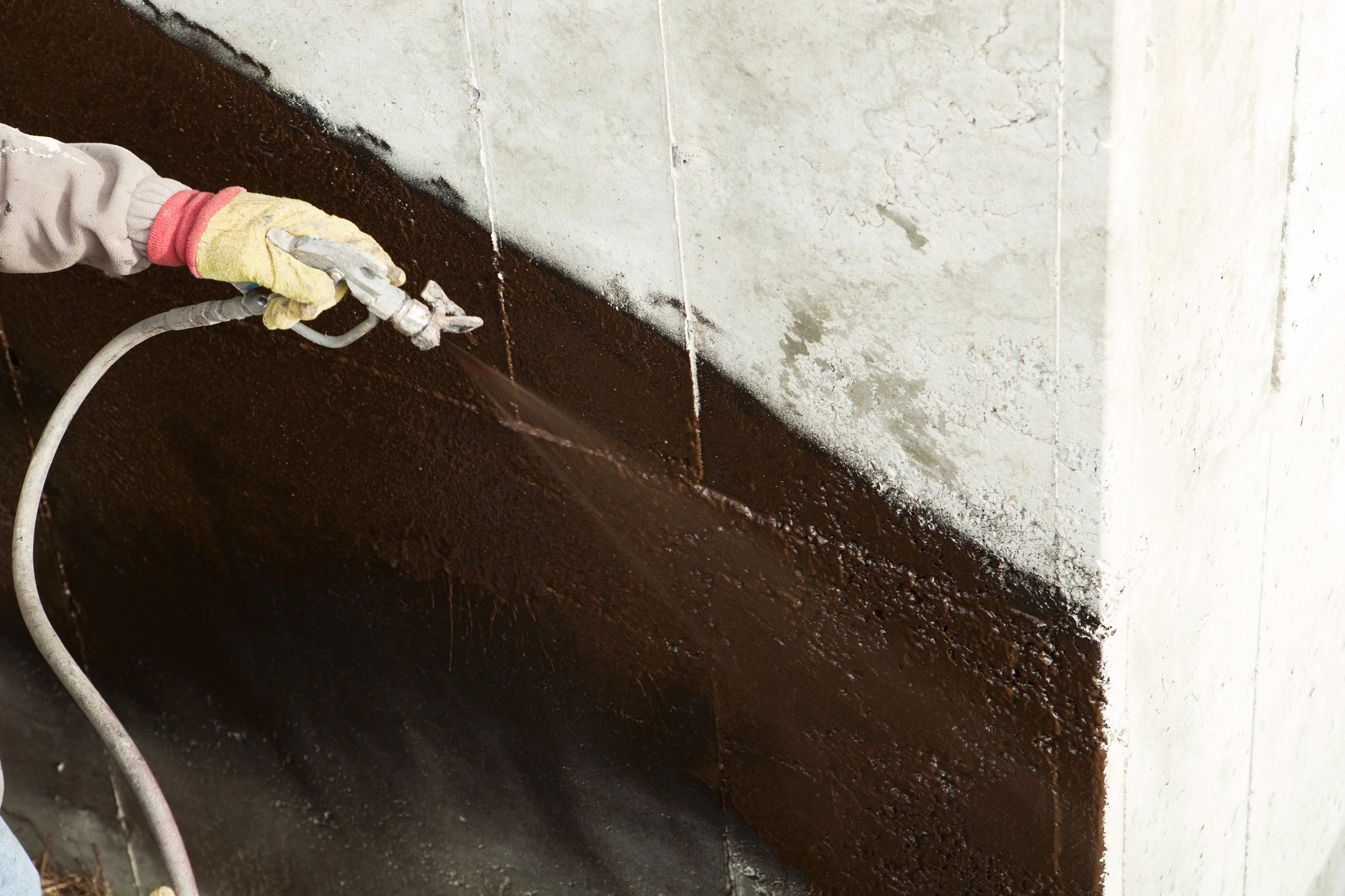 Spraying waterproofing material on foundation wall.