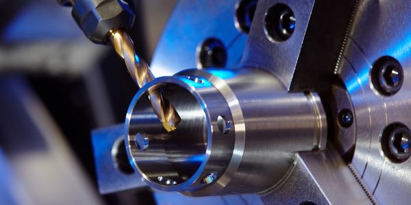 Close-up of a drill bit machining a cylindrical metal part.
