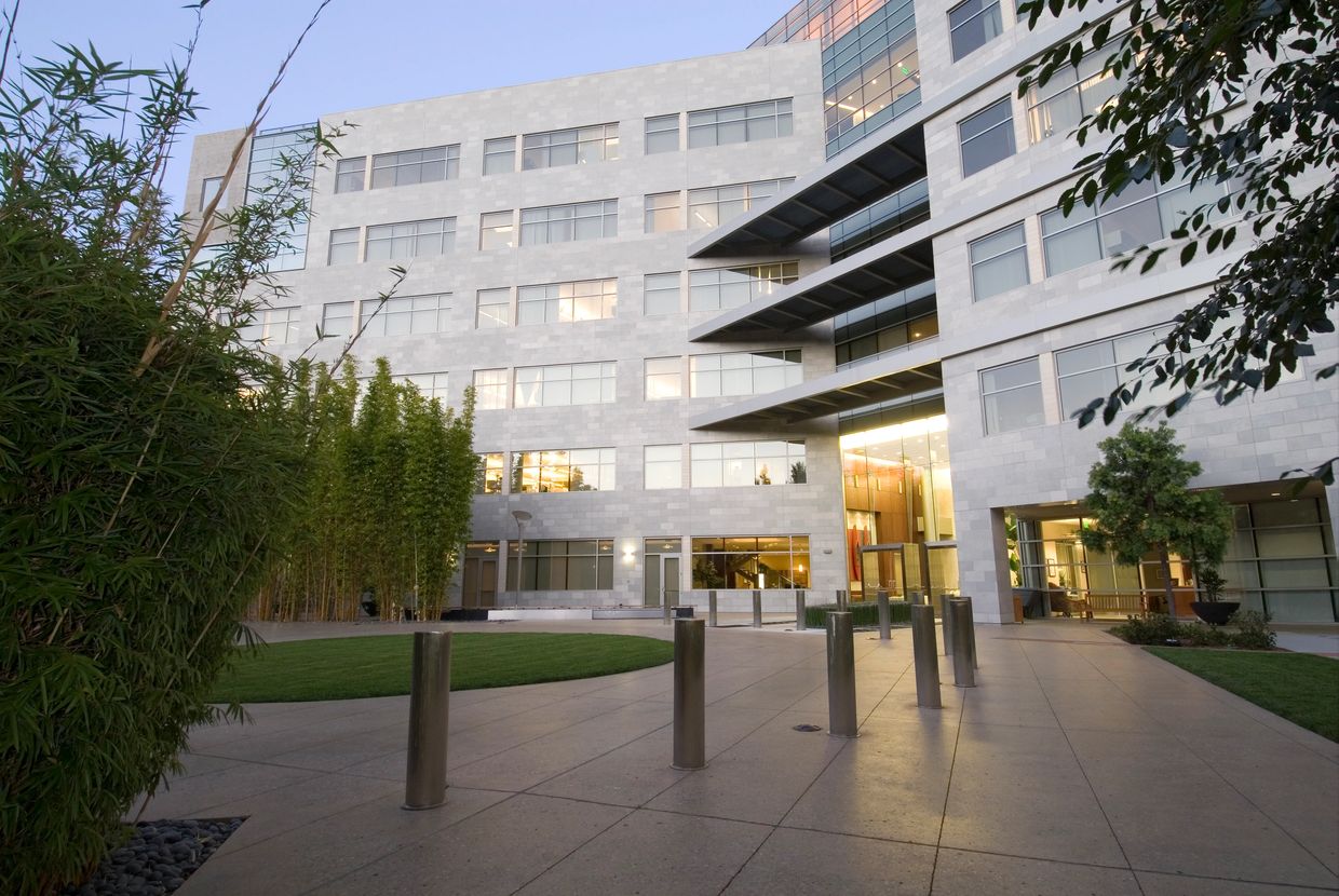 Modern office building with large windows and greenery at the entrance.