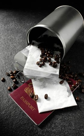 Spilled coffee beans from a metal tin onto a passport and dark surface.