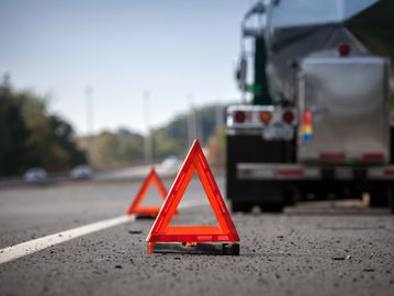 Two red emergency warning triangles placed on a road near a stopped tanker truck.