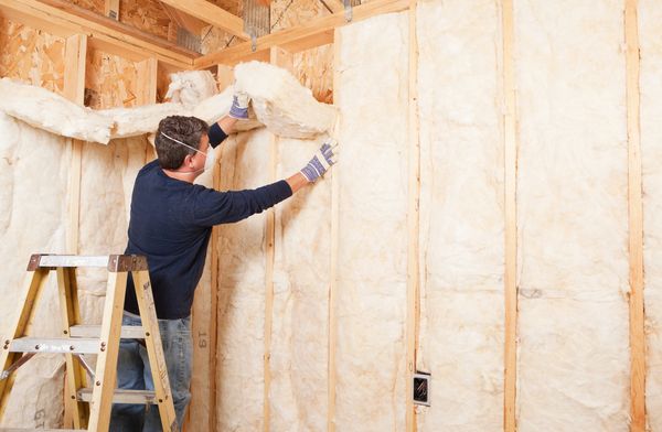 Man installing fiberglass insulation inside wall studs.