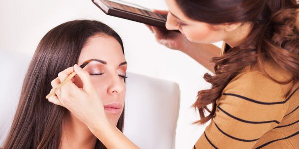 A makeup artist applying eyeshadow to a woman's eyelid with a brush.