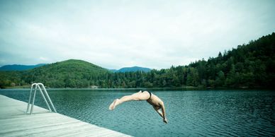 Man diving into a lake from a wooden dock surrounded by forested hills.