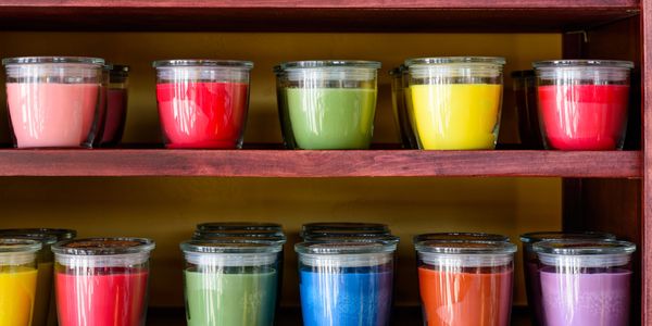 Colorful candles in glass jars arranged on wooden shelves.
