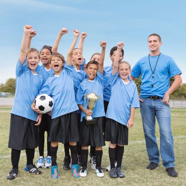 Youth soccer team celebrating victory with trophy and coach.