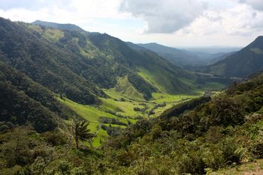 Lush green valley surrounded by forested mountains under a cloudy sky.