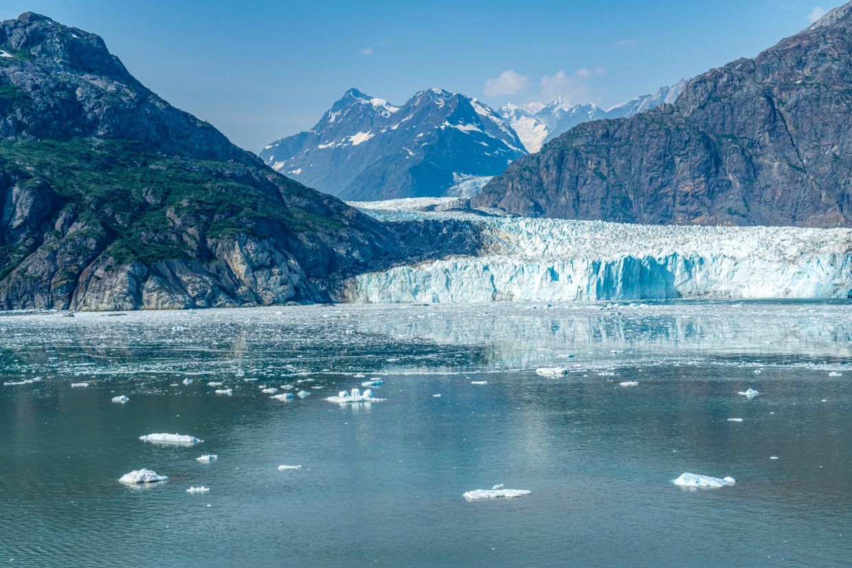 A glacier surrounded by mountains with floating ice chunks in calm water.