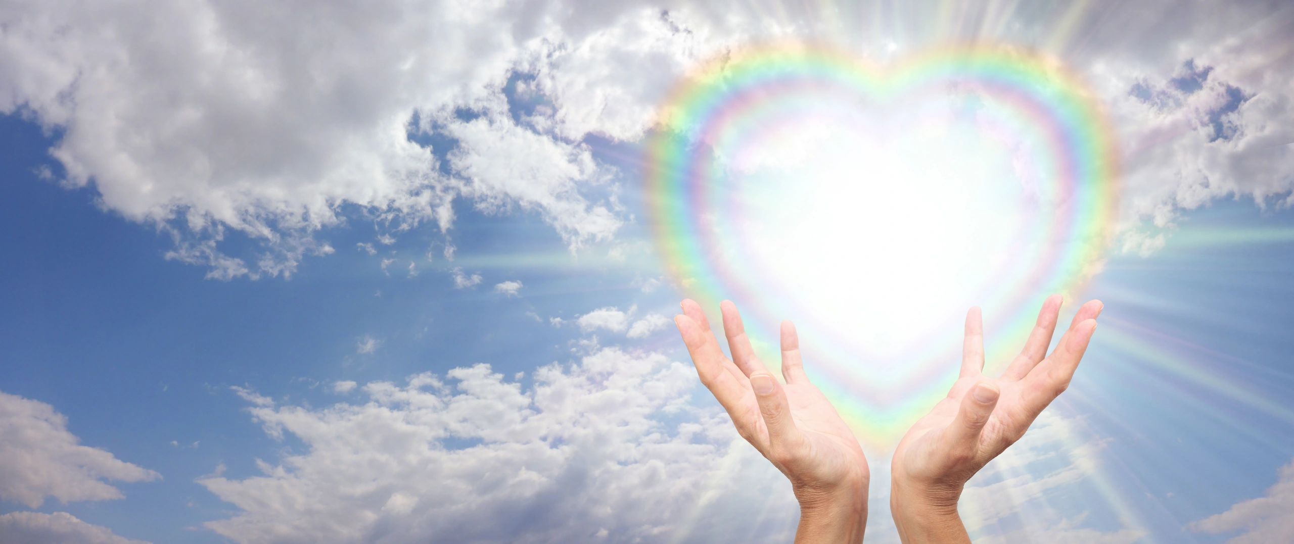 Hands reaching towards a glowing heart-shaped rainbow in the sky.