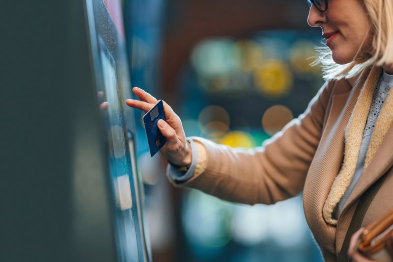 A side view of a smiling Caucasian female holding her credit card while using cash machine.
