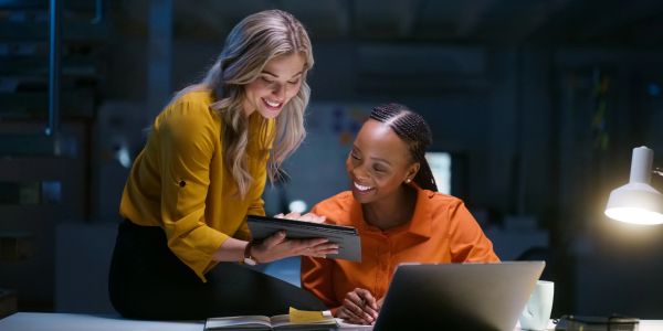 Two women happily collaborating over a tablet in a workspace.