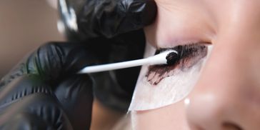 Applying eyelash extension adhesive with a cotton swab.