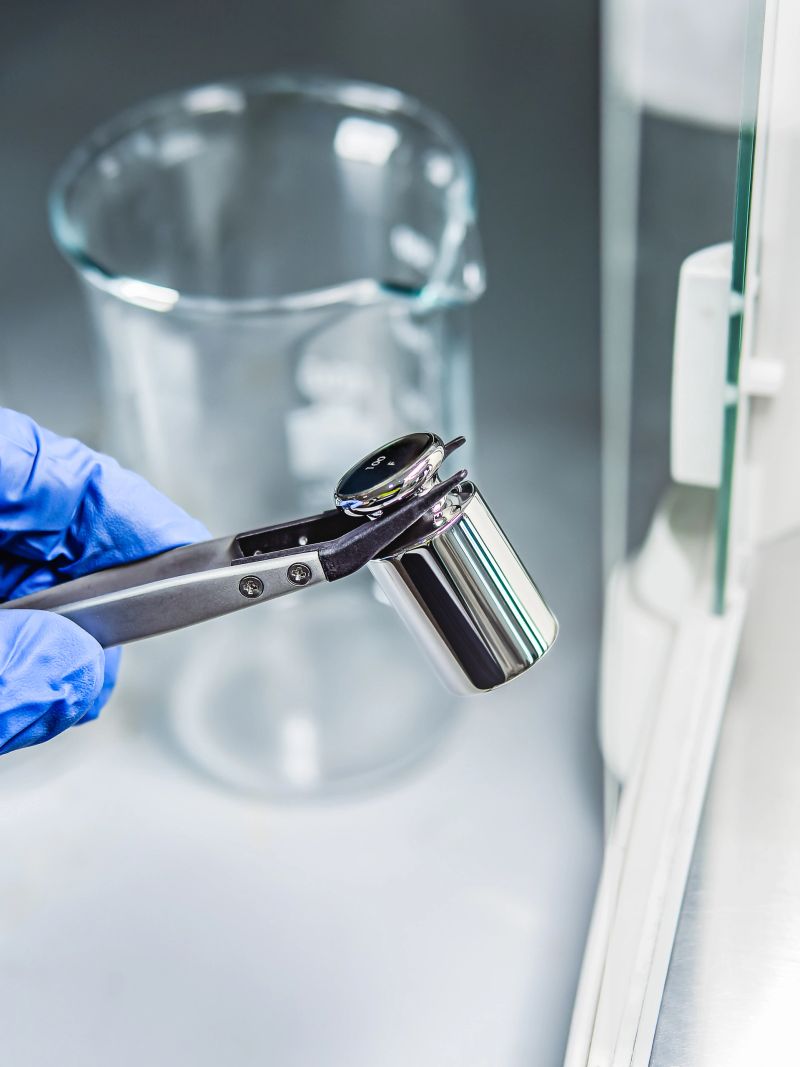 A operator's hand is holding steel calibration weight to place on the analytical balance. Concept of quality control in a laboratory.