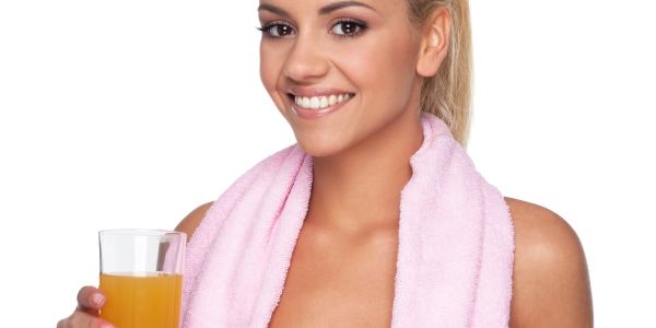 Smiling woman with a pink towel holding a glass of orange juice.