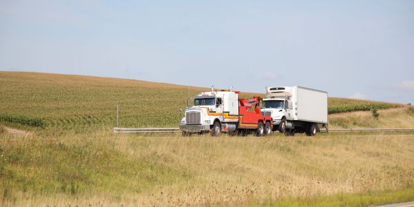Tow truck hauling a white box truck on a rural road.