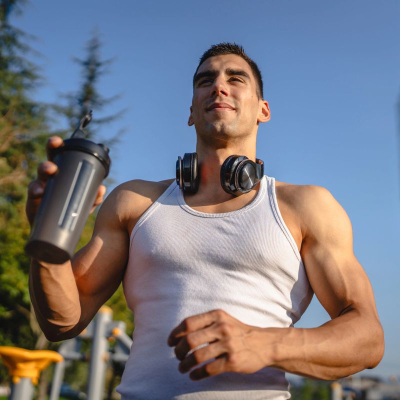 One caucasian man young male athlete take a brake during outdoor training in the park outdoor gym hold supplement shaker in hand happy confident strong copy space
