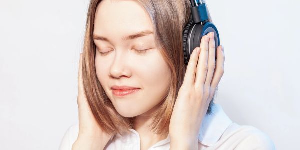 Mulher ouvindo música com fones de ouvido e olhos fechados.