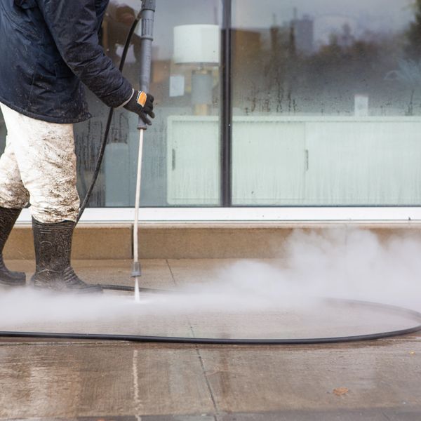 Worker power washing a concrete surface outside a building.