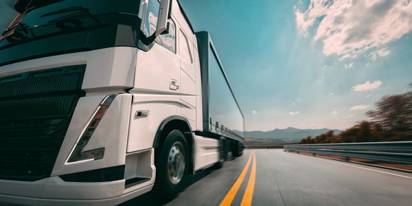 White semi-truck speeding on a curved highway under a clear sky.